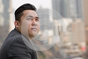 Closeup profile view of young overweight Asian businessman thinking in the city