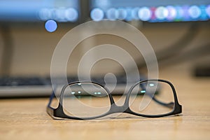 Closeup of protective glasses on an empty desk with blurred computer screen on background