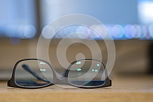 Closeup of protective glasses on an empty desk with blurred computer screen on background
