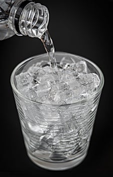 Closeup of puring water Into glass with ice on dark background