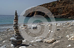 Closeup of pyramid of stones on sandy beach with stones. Blue sea, coastline and rocky mount. Stone symbol