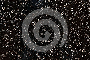 Closeup of rain water drops behind glass at evening. It looks like bubbles in black liquid. Abstract wet background