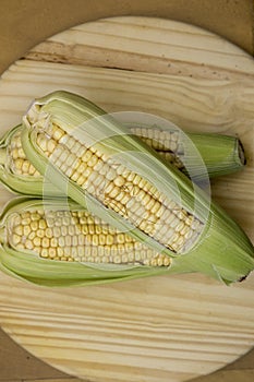 Closeup of raw corn cobs with straw over wood