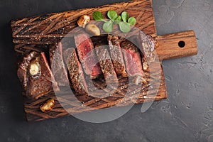 Closeup ready to eat steak new York beef breeds of black Angus with herbs, garlic and butter on a wooden Board. The finished dish