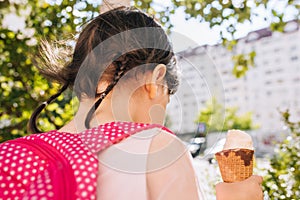 Closeup rear view of cute little girl eating ice cream with blurred buildings outdoor. Happy kid toodler girl relaxing after