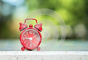 Closeup red alarm clock display seven hours and fifteen minutes on screen on blurred marble desk and park view background