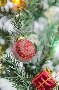 Closeup of red ball hanging from a decorated Christmas tree.