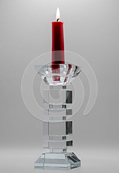 Closeup of a red candle in clear glass candelabra against the grey background