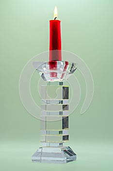 Closeup of a red candle in clear glass candelabra against the light green background