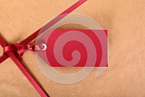 Closeup red gift tag and ribbon, brown parcel wrapping paper background