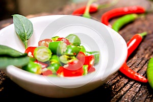 Closeup Red and green chili with chili sliced in the white small bowl on wooden table