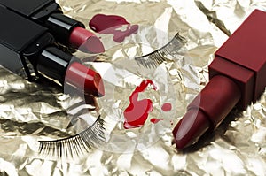 Closeup of red lipsticks, eyelashes and spilled nail polish on the shine golden surface.Concept of beautiful and glam makeup