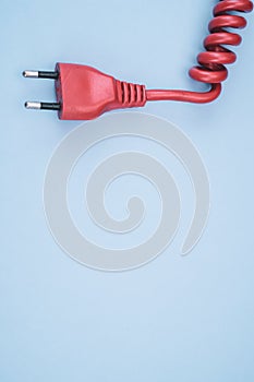 Closeup of a red networking cable with an electric plug on a light blue background