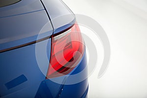 Closeup of a red tail light of a blue luxury car isolated on a grey background