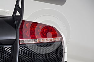 Closeup of a red tail light of a white luxury car isolated on a grey background