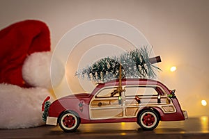 Closeup of red toy car carrying a Christmas tree next to a Santa hat
