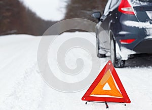 Closeup of red warning triangle with a broken down car