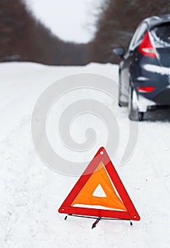 Closeup of red warning triangle with a broken down car