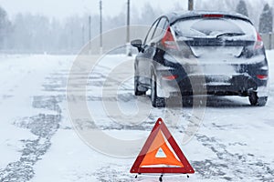 Closeup of red warning triangle with a broken down car in winter