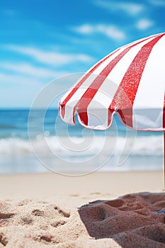 Closeup a red and white striped beach umbrella on a background of a summer beach with sun loungers and blue sea or ocean, vertical