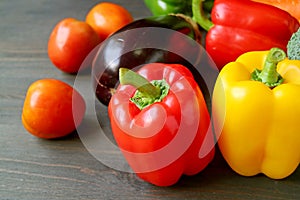 Closeup of red and yellow bell peppers with another colorful fresh vegetables on a wooden table