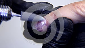 Closeup of removing nail cuticles and fingernail polishing using electric manicure drill machine.
