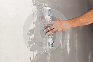 Closeup of repairman hand plastering a wall with putty knife or spatula.