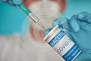 Closeup of a researcher with face mask and blue gloves filling a syringe with coronavirus vaccine