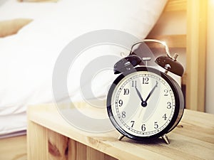 Closeup retro alarm clock on Bedside table with bed background