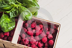 Closeup of a ripe juicy berry raspberry in a wicker basket with green basil leaves