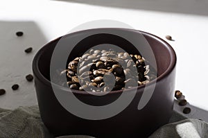 Closeup of roasted coffee beans in the brwn bowl standing on the white table, morning light from window