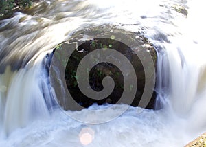 Closeup of a rock dividing a small cascade of water at a river