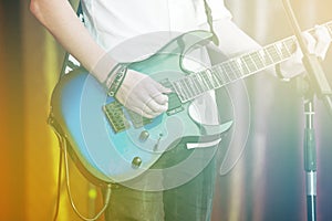 Closeup rockstar on stage playing on electro guitar. Male guitarist in a white shirt