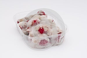 Closeup of rotten moldy raspberry in plastic box  on white