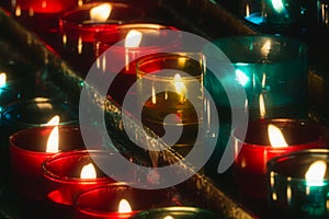 Closeup of rows of candles burning in multicolored glass tealights in a church Selective focus