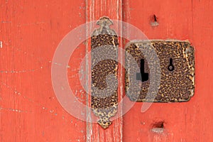 Closeup of rusted antique keyhole and lock on red wooden door