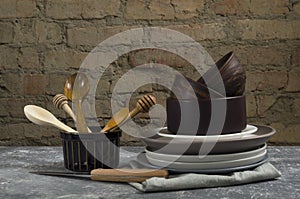 Closeup of rustic kitchenware, utensil on the table against old brick wall.Woodn spoons, clay and ceramic plates, bowls, napkin on