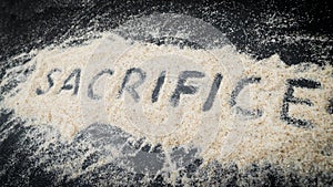 Closeup of SACRIFICE word written on white sand