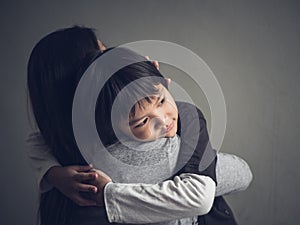 Closeup sad little boy being hugged by his mother at home.