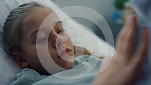 Closeup sad little patient touching soft toy in ward. Sick kid missing parents.