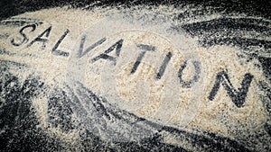 Closeup of SALVATION text written on white sand