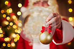 Closeup of Santa Claus hands with christmas ball decoration, sitting indoor near decorated xmas tree with lights - Merry Christmas