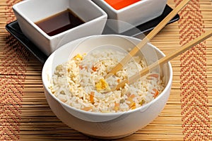 Closeup of sauces and a bowl of cooked rice with vegetables and chopsticks on the table