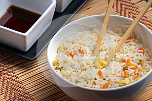 Closeup of sauces and a bowl of cooked rice with vegetables and chopsticks on the table