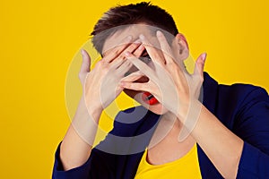 Closeup scared woman covering face with hands hiding face looking peering peeking through fingers on yellow background. Family