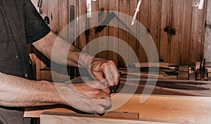 Closeup scene of a male carpenter working in carpentry workshop, planing a wood piece with a double hand push woodworking bird pla