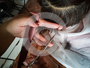 Closeup scissor on hand hair stylist. Cutting black short hair of Asian woman.