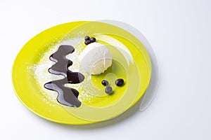 Closeup of a scoop of vanilla ice cream on a yellow plate with powdered sugar, chocolate syrup