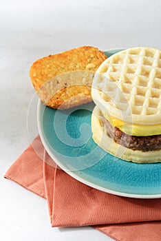 Closeup of scrambled egg sausage waffle sandwich with hash brown