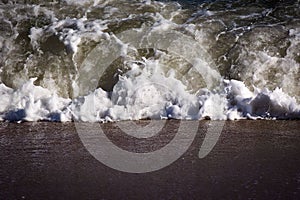 Closeup of the sea foaming waves rolling sandy ashore in the daytime